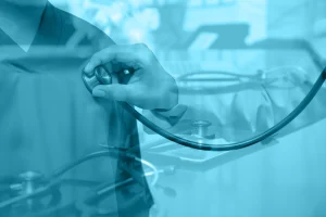A healthcare professional using a stethoscope on a patient's chest, with a blurred clinical setting in the background.