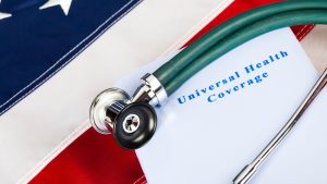 Stethoscope resting on a document titled "Universal Health Coverage," placed on a backdrop of a United States flag.