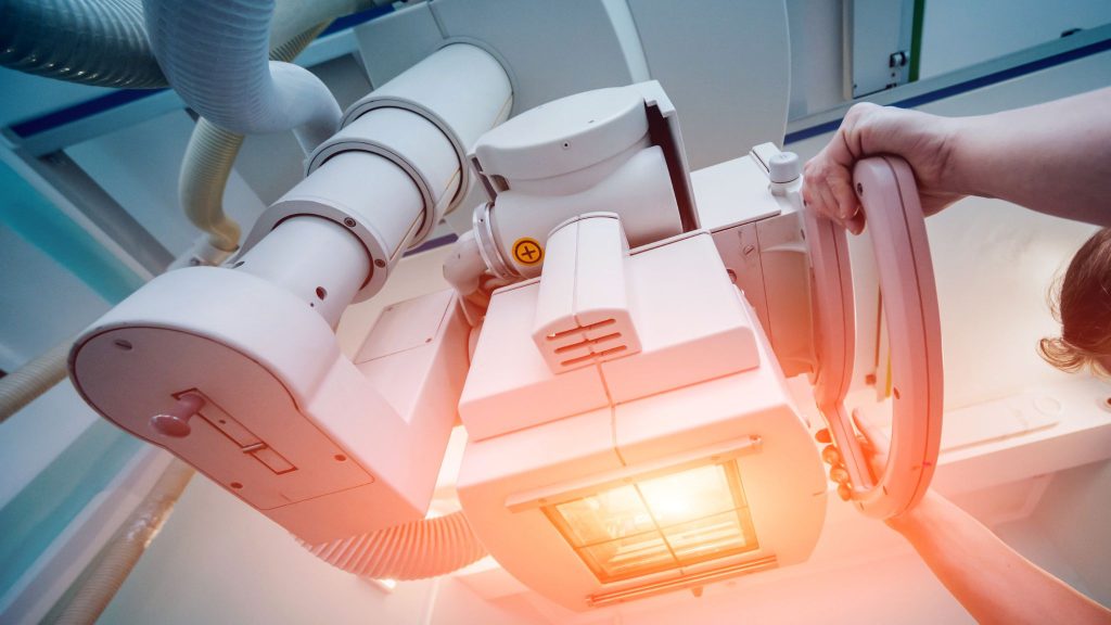 A close-up view of a medical imaging device with a person adjusting it, showing control knobs and an illuminated part of the machine.