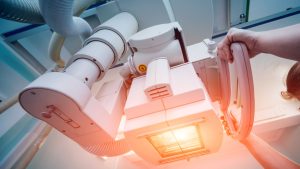 A close-up view of a medical imaging device with a person adjusting it, showing control knobs and an illuminated part of the machine.