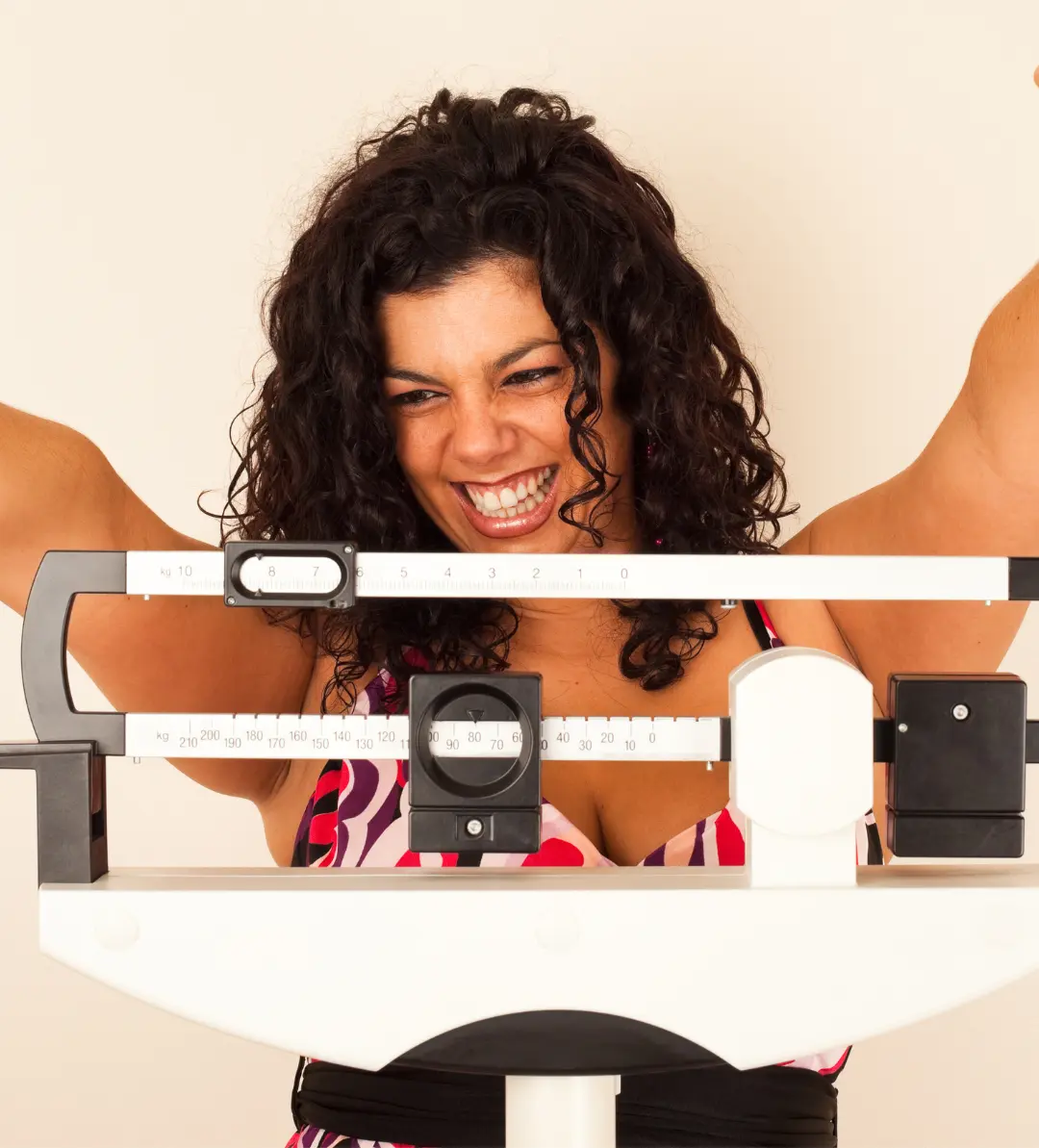 Smiling woman raising her arms in celebration while standing on a scale, representing successful weight management and healthy lifestyle progress